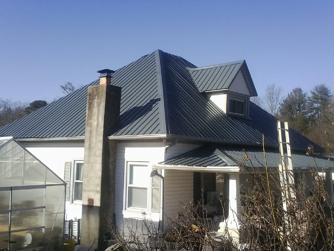 Dark blue standing seam metal roof on a white farmhouse with dormer — Slate & Tile Roof Repair by Roofing Brothers in Bronson