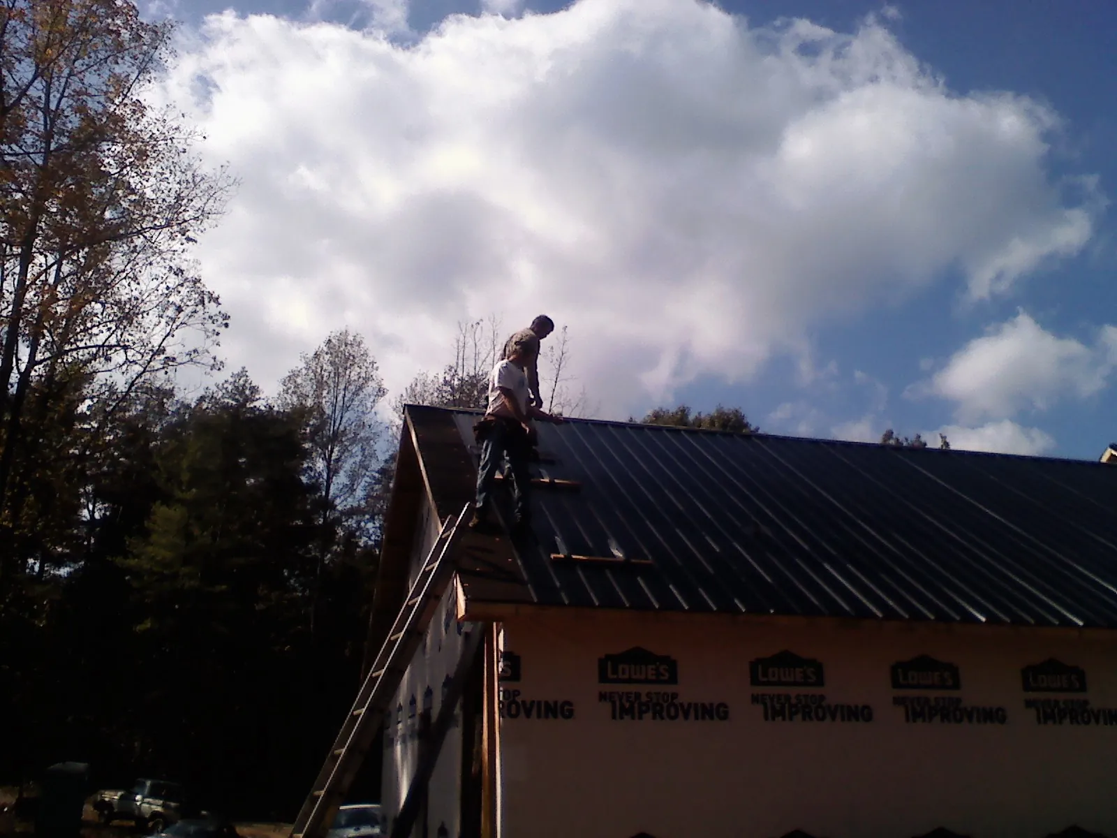 Roofer fastening dark metal panels high against a cloudy sky, from a Roof Inspection job in Bronson